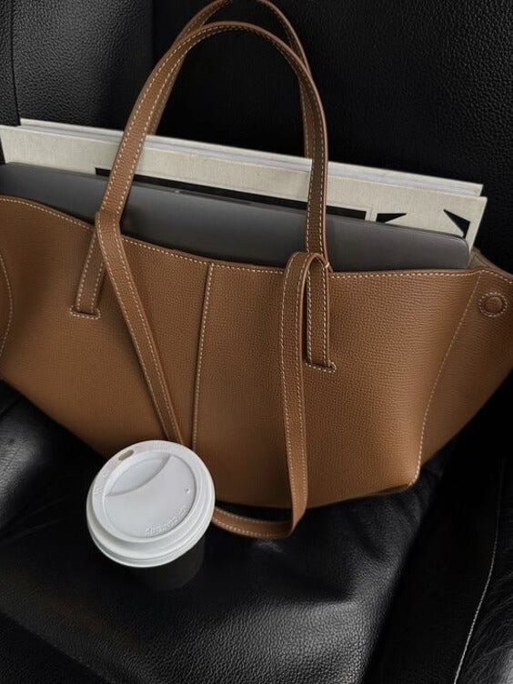 Borsa in pelle marrone su sedile auto con caffè da asporto e laptop. Accessori moda eleganti, borsa capiente, stile urbano.