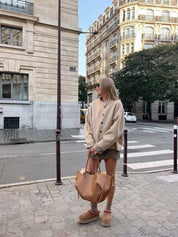 Donna con cardigan beige e borsa marrone in strada cittadina, moda autunnale, abbigliamento casual chic, edifici storici sullo sfondo.