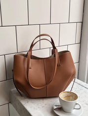 Borsa a mano in pelle marrone su tavolo di marmo bianco, accanto a tazza di caffè. Elegante accessorio moda donna, design moderno e raffinato.