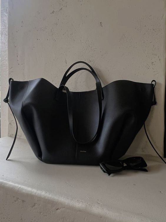 Borsa tote nera in pelle su sfondo chiaro, design elegante e moderno, accessorio di moda, occhiali da sole neri accanto.