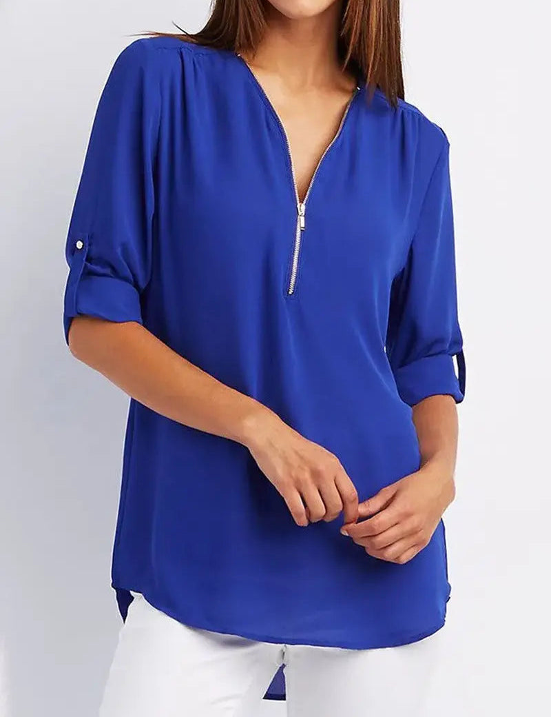 Donna con blusa blu elettrico a maniche lunghe, scollo a V con zip, abbinata a pantaloni bianchi. Moda casual elegante, abbigliamento femminile.