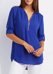Donna con blusa blu elettrico a maniche lunghe, scollo a V con zip, abbinata a pantaloni bianchi. Moda casual elegante, abbigliamento femminile.