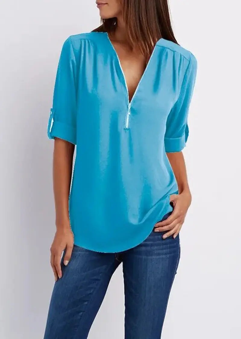 Blusa azzurra da donna con scollo a V e zip, maniche a 3/4 arrotolate, abbinata a jeans. Moda casual elegante, abbigliamento femminile trendy.