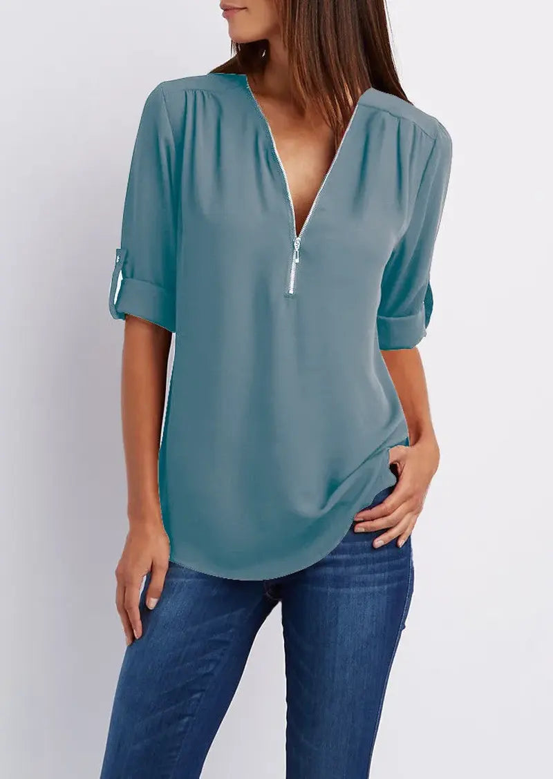 Blusa donna azzurra con zip frontale, maniche a 3/4 arrotolate, abbinata a jeans. Moda casual elegante, tessuto leggero, stile versatile.