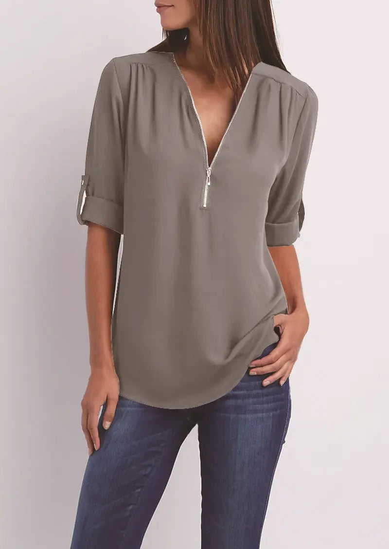 Blusa donna grigia con zip frontale, maniche a 3/4 arrotolate, scollo a V, abbinata a jeans. Moda casual elegante, abbigliamento femminile.