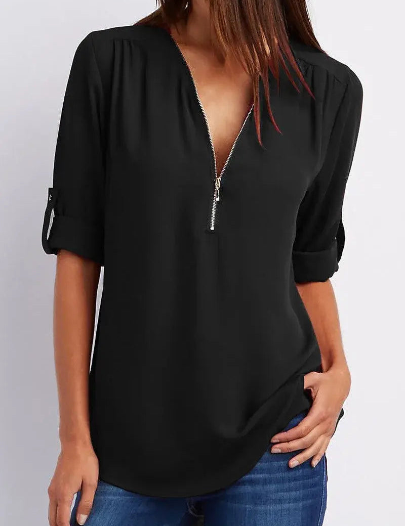 Donna con camicetta nera a maniche lunghe, scollo a V con zip, abbinata a jeans blu. Moda casual elegante, abbigliamento femminile trendy.