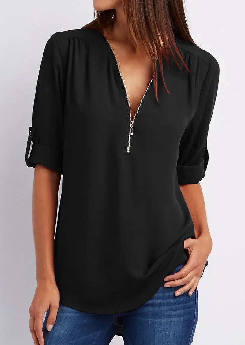 Donna con camicetta nera a maniche lunghe, scollo a V con zip, abbinata a jeans blu. Moda casual elegante, abbigliamento femminile trendy.