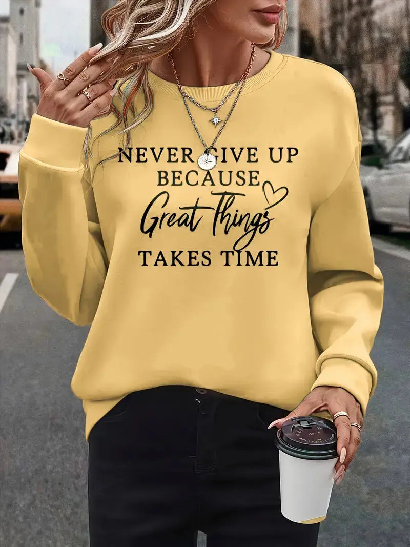 Donna con felpa gialla con scritta motivazionale, collane a strati, pantaloni neri, tiene bicchiere di caffè. Moda casual autunnale urbana.