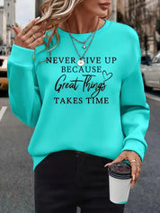 Donna con felpa turchese con scritta motivazionale, collane dorate e caffè da asporto. Moda casual, abbigliamento autunnale, ispirazione quotidiana.
