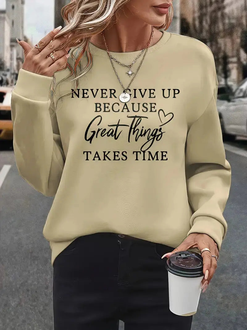 Donna con maglione beige con scritta motivazionale, collane a strati, pantaloni neri, tiene una tazza da caffè. Moda casual autunnale urbana.