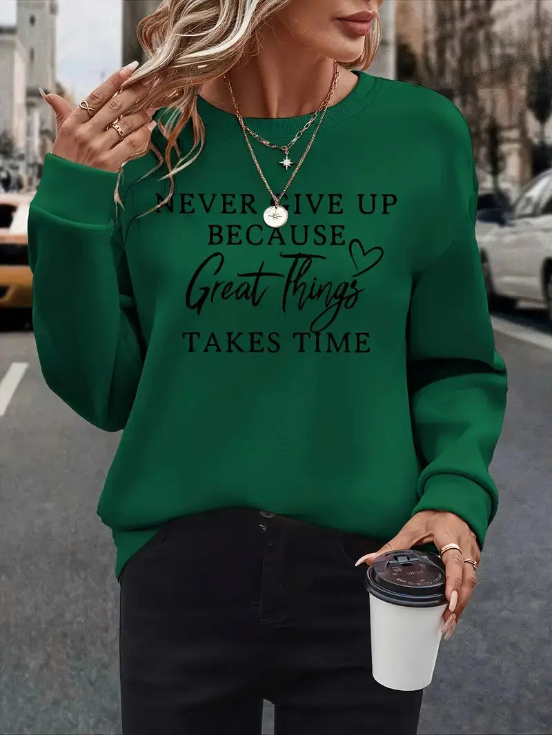 Donna con maglione verde con scritta motivazionale, collane dorate, pantaloni neri, tiene una tazza da caffè. Moda casual autunnale urbana.