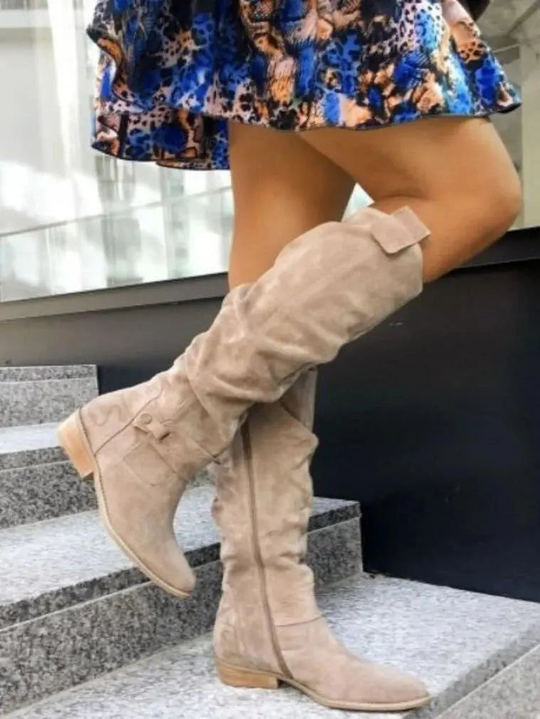 Stivali alti beige in camoscio su gradini, abbinati a gonna colorata. Scarpe moda donna, stile autunnale, tacco basso, eleganti e casual.