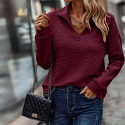 Donna con maglione bordeaux a coste, jeans blu e borsa a tracolla nera trapuntata. Moda autunnale casual elegante.