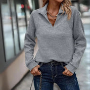 Donna con maglione grigio a righe, zip frontale, jeans blu, collana dorata. Moda casual autunnale, abbigliamento femminile trendy.