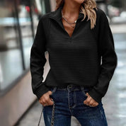 Donna con maglione nero a coste, zip frontale, indossa jeans blu. Moda casual autunnale, abbigliamento femminile elegante e confortevole.
