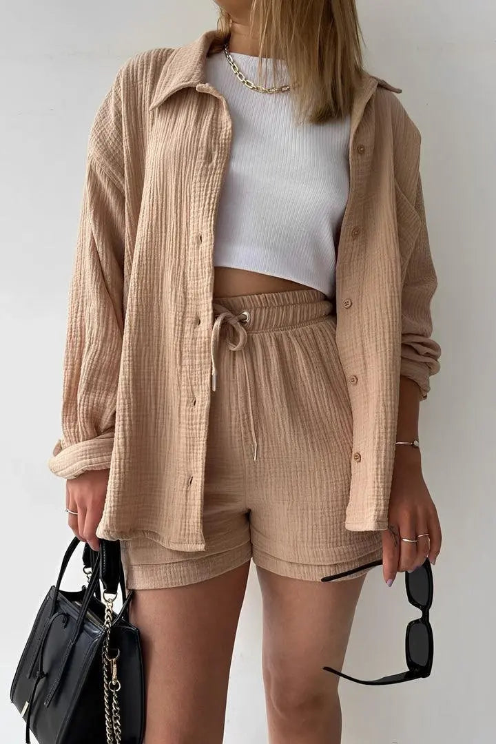 Donna con camicia beige e pantaloncini coordinati, top bianco, borsa nera e occhiali da sole. Moda casual estiva, abbigliamento femminile trendy.
