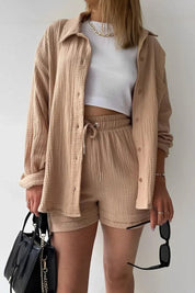 Donna con camicia beige e pantaloncini coordinati, top bianco, borsa nera e occhiali da sole. Moda casual estiva, abbigliamento femminile trendy.