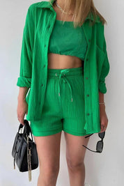 Donna con completo verde a tre pezzi: camicia, top e shorts. Accessori: borsa nera e occhiali da sole. Moda estiva, abbigliamento casual chic.