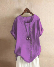 Blusa viola in lino con bottoni decorativi, maniche corte e scollo rotondo, appesa su gruccia. Abbigliamento estivo casual donna.