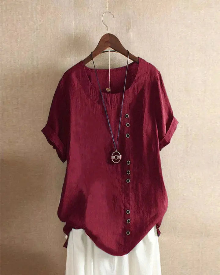 Blusa rossa in lino con bottoni decorativi, maniche corte e scollo rotondo, appesa su gruccia. Design casual ed elegante per donna.