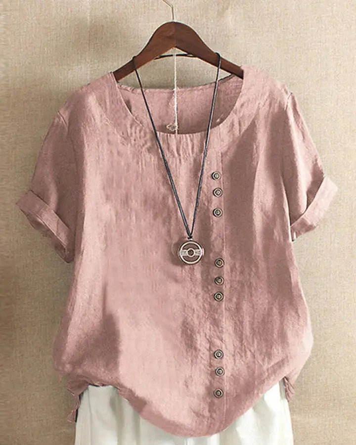 Camicia donna in lino rosa con bottoni decorativi, maniche corte risvolte, abbinata a collana pendente. Stile casual elegante.