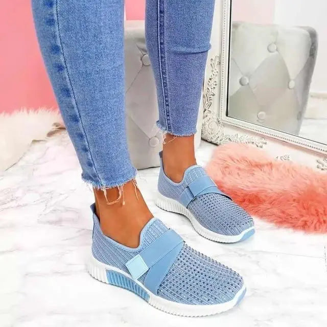 Scarpe da ginnastica blu da donna con suola bianca, indossate con jeans aderenti. Design moderno e casual, perfette per lo stile quotidiano.