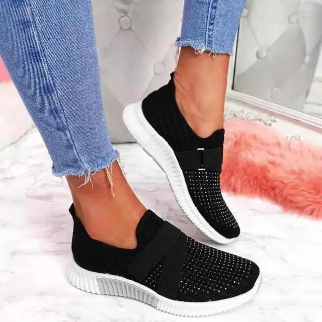 Scarpe da ginnastica nere da donna, design slip-on, suola bianca, indossate con jeans. Scarpe casual eleganti, comode e traspiranti.