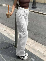 Donna con pantaloni cargo bianchi e top marrone, tiene un caffè freddo. Scarpe da ginnastica bianche e nere. Moda casual urbana.
