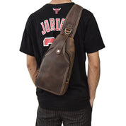 Zaino a tracolla in pelle marrone su uomo con maglietta nera. Design elegante, ideale per viaggi e uso quotidiano. Accessorio moda maschile.