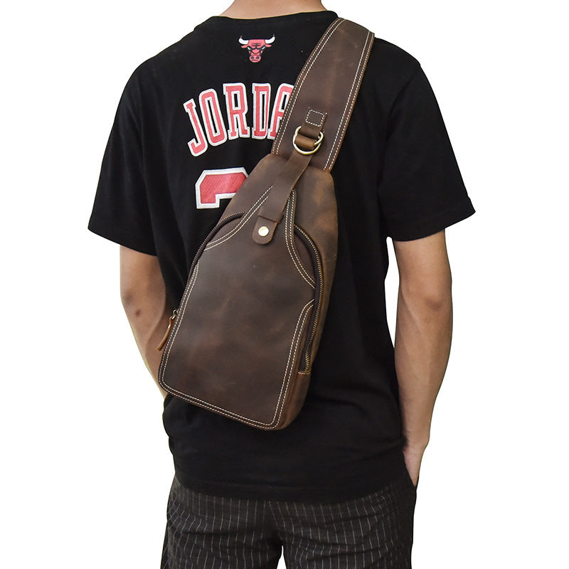 Zaino a tracolla in pelle marrone su uomo con maglietta nera. Design elegante, ideale per viaggi e uso quotidiano. Accessorio moda maschile.