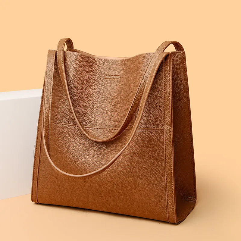 Borsa tote in pelle marrone chiaro su sfondo beige, design elegante e minimalista, ideale per moda donna, accessorio versatile e di tendenza.