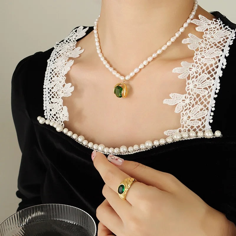 Collana di perle con ciondolo verde su abito nero con colletto in pizzo bianco, anello coordinato, moda elegante, accessori gioielli donna.