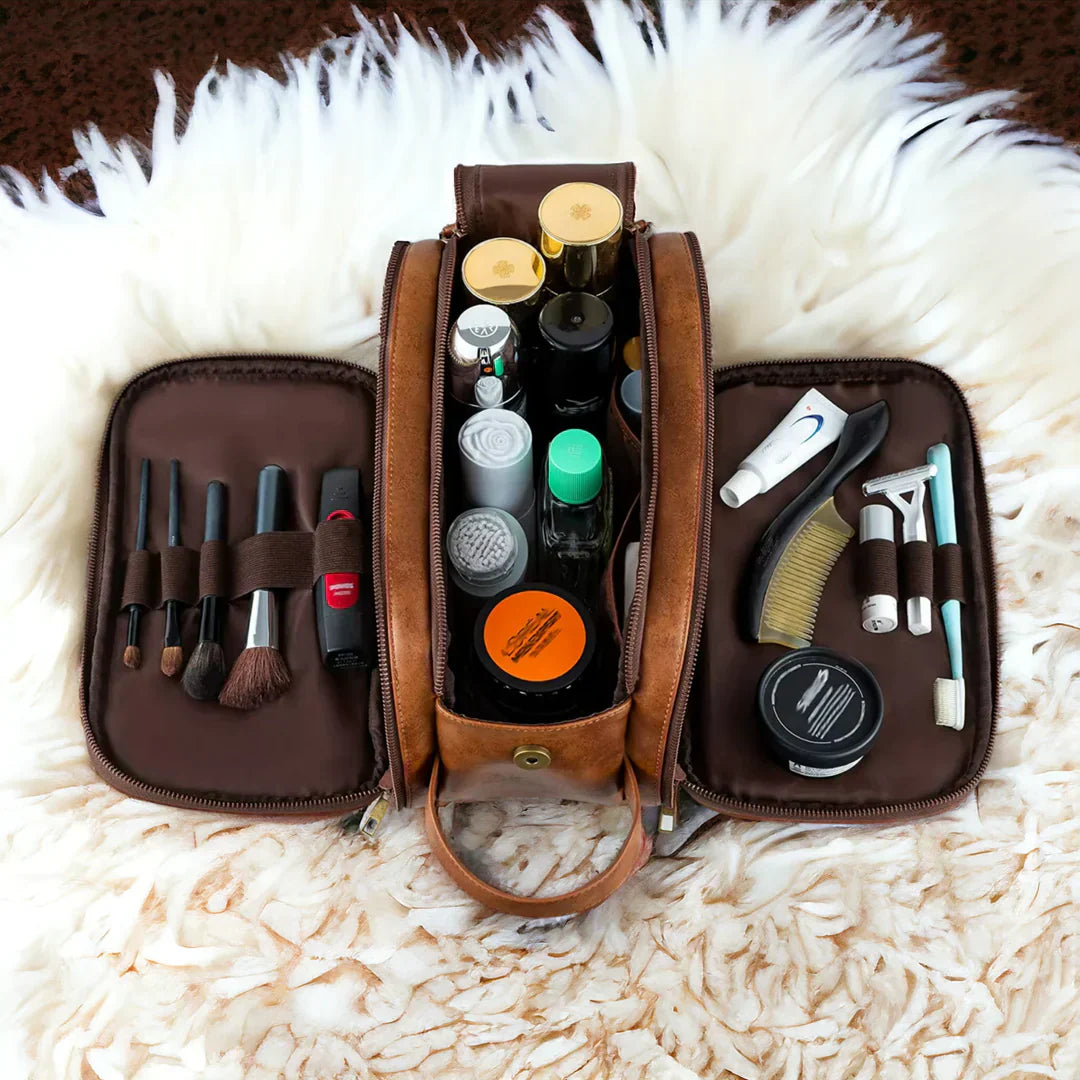 Beauty case in pelle marrone aperto su tappeto bianco, contenente pennelli trucco, flaconi cosmetici, rasoio e accessori per la cura personale.