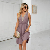 Abito estivo donna viola con scollo a V e dettagli in pizzo, indossato da modella bionda con occhiali da sole, borsa beige, sfondo interno elegante.