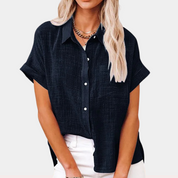 Camicia donna nera a maniche corte, tessuto leggero, colletto classico, abbinata a pantaloni bianchi. Stile casual elegante, moda estiva.
