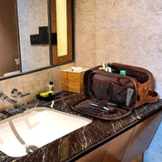 Borsa da toilette in pelle marrone su lavabo in marmo, con scomparti aperti contenenti articoli da toeletta. Accessori bagno eleganti e funzionali.