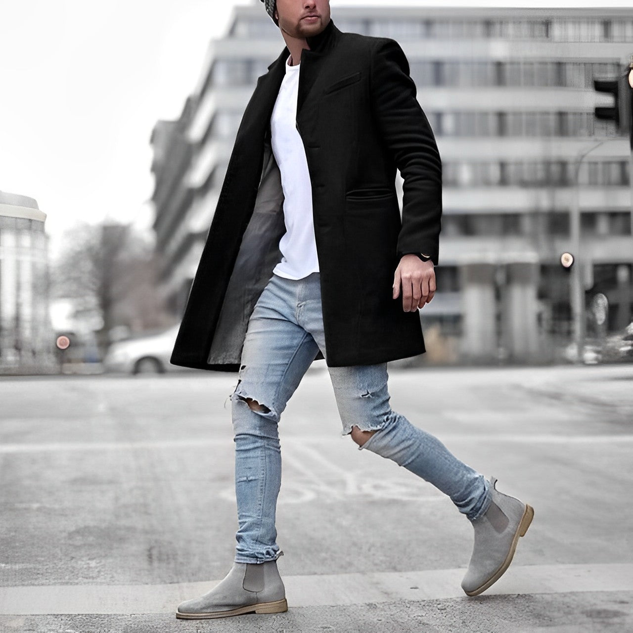 Uomo con cappotto nero elegante, jeans strappati azzurri e stivali grigi, cammina in città moderna. Moda urbana, abbigliamento invernale maschile.