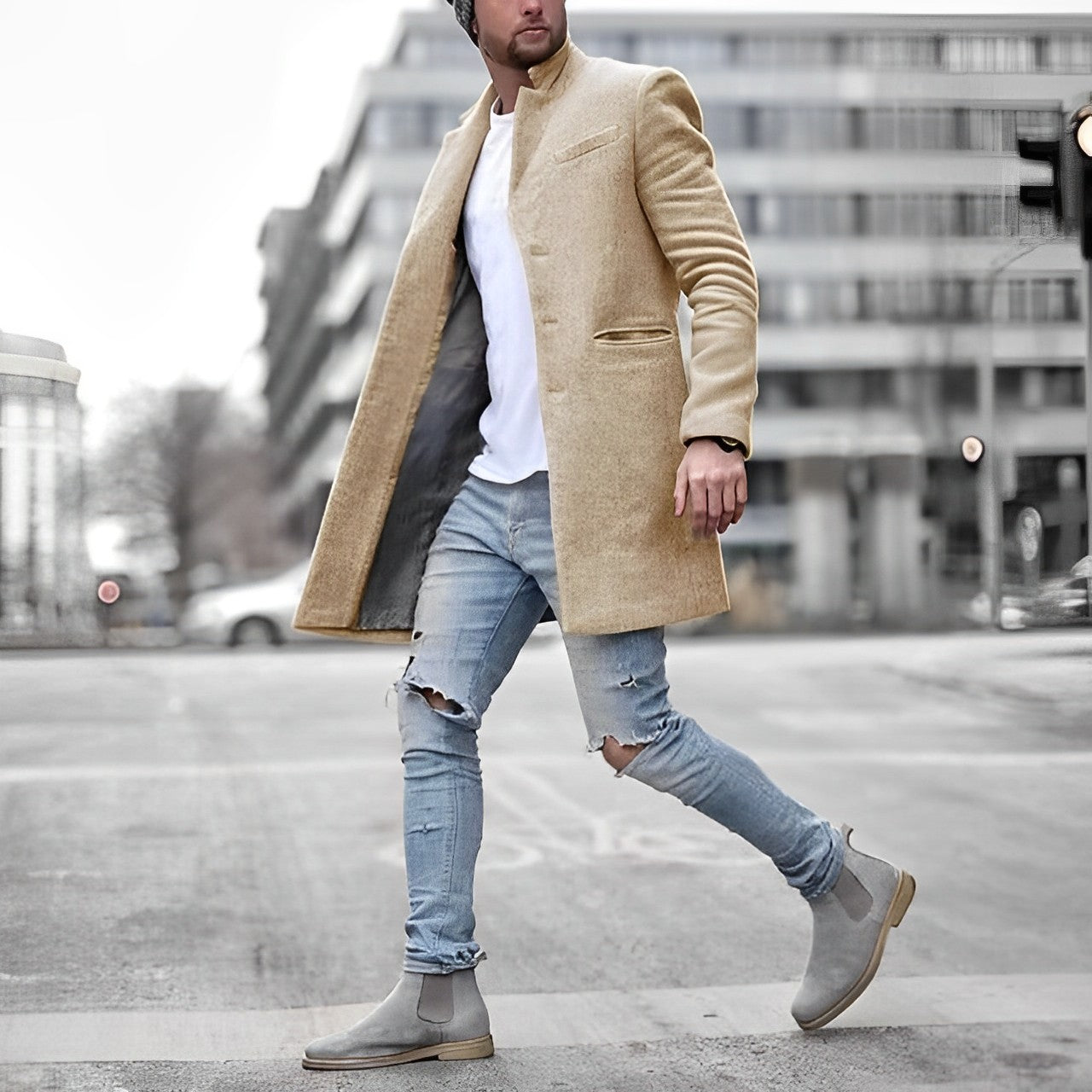 Uomo alla moda con cappotto beige, jeans strappati e stivali grigi cammina in città. Look urbano elegante, abbigliamento invernale maschile.