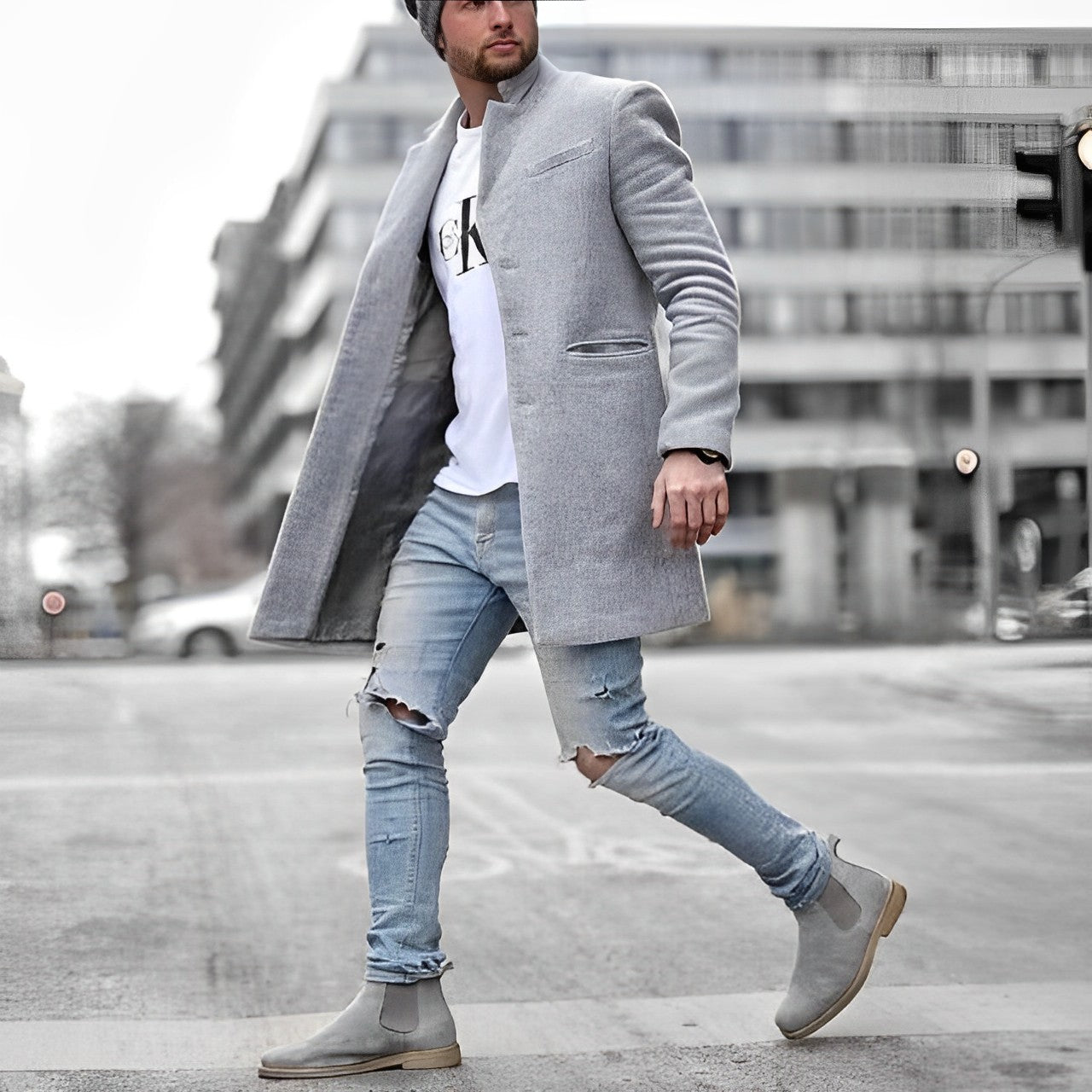 Uomo con cappotto grigio elegante, jeans strappati e stivali Chelsea grigi cammina in città. Moda maschile urbana, stile casual chic.