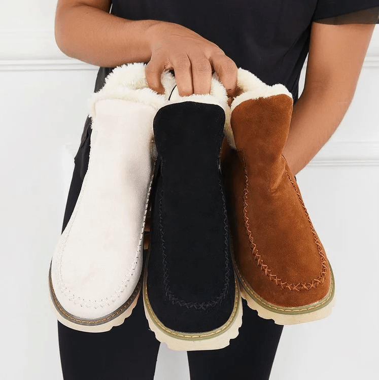 Donna che tiene stivali invernali in pelle scamosciata, colori bianco, nero e marrone, con fodera in pelliccia. Scarpe calde e alla moda per l'inverno.