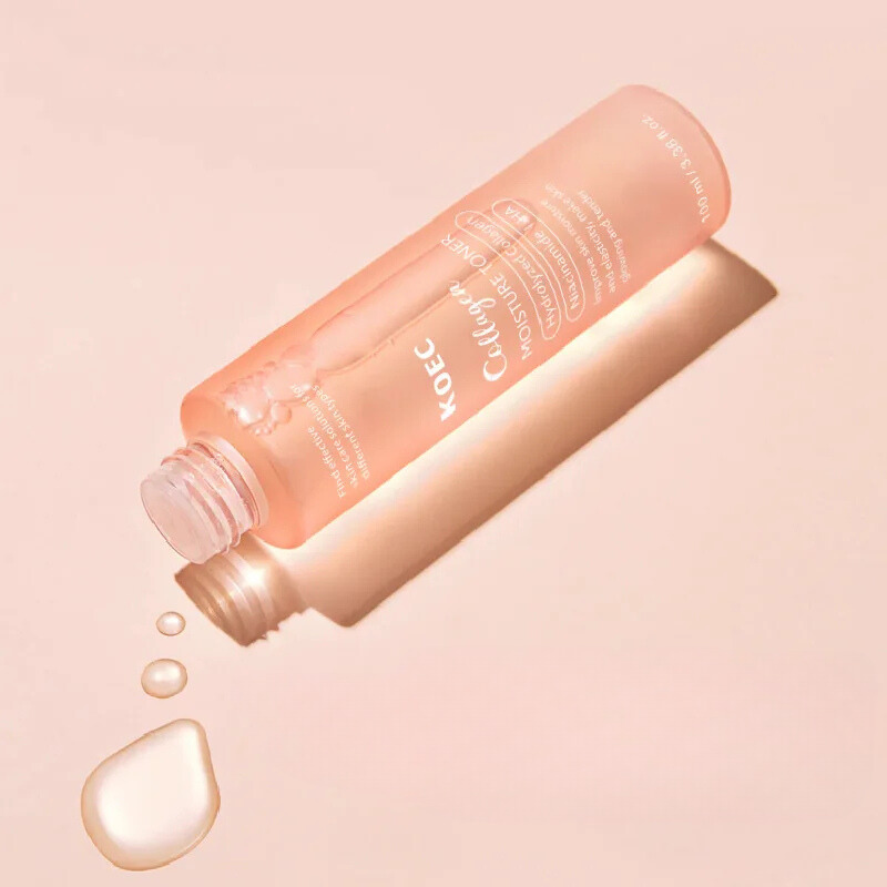 Bottiglia di tonico viso rosa su sfondo beige, con gocce d'acqua. Skincare idratante, bellezza, cura della pelle, cosmetici coreani.