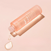 Bottiglia di tonico viso rosa su sfondo beige, con gocce d'acqua. Skincare idratante, bellezza, cura della pelle, cosmetici coreani.
