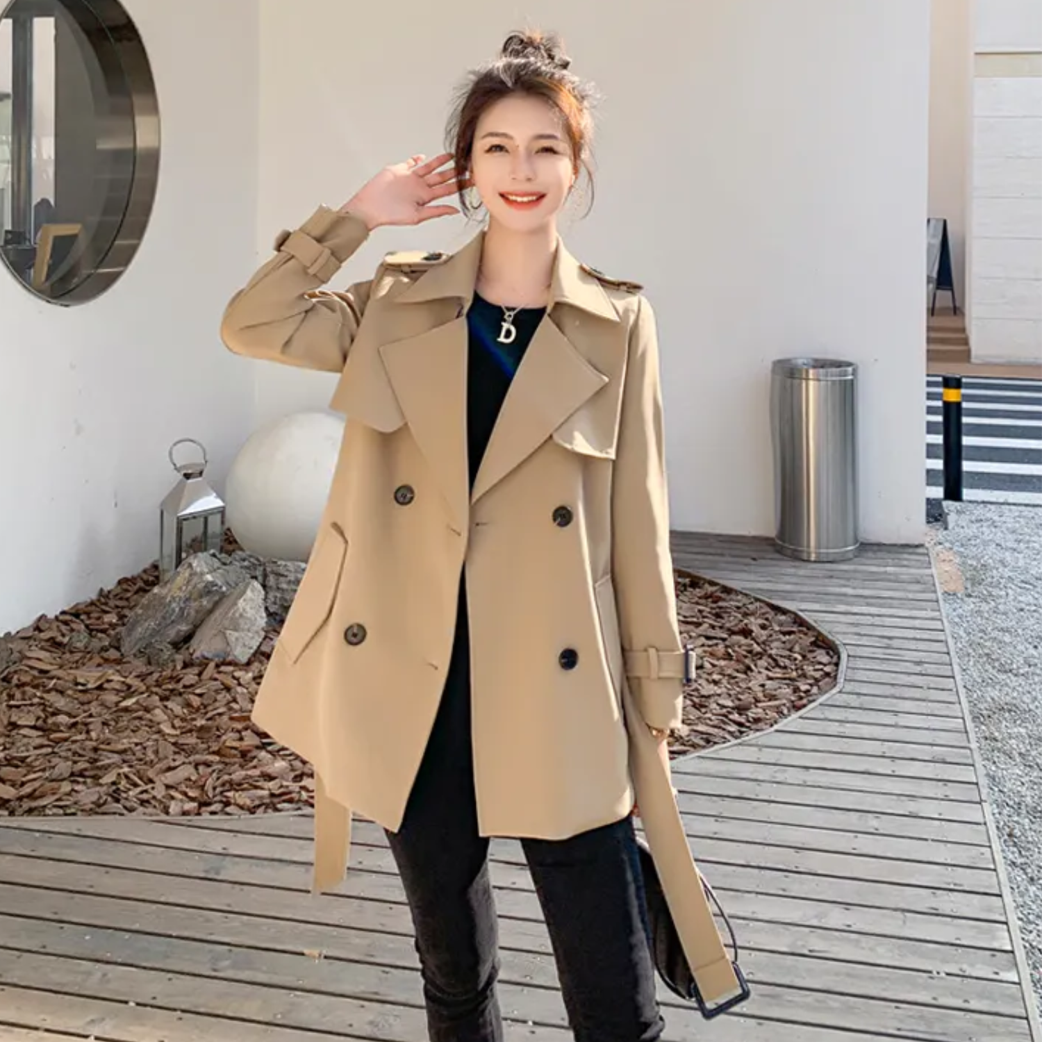 Donna con trench beige, doppio petto, cintura in vita, posa all'aperto. Moda autunnale, cappotto elegante, abbigliamento casual chic.