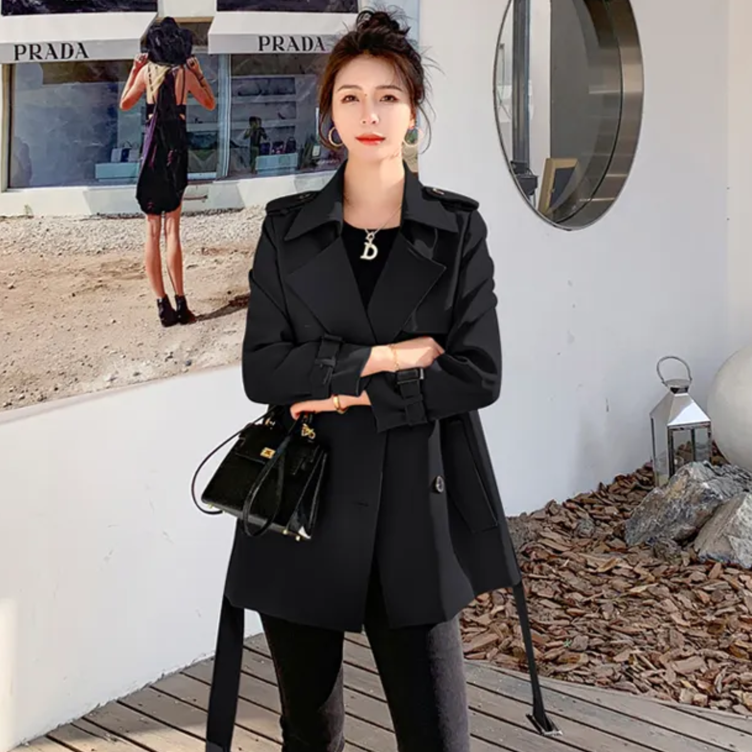 Donna con cappotto nero elegante, borsa a tracolla, davanti a negozio di moda. Stile autunnale, abbigliamento femminile chic, tendenze moda 2023.
