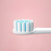 Testina di spazzolino elettrico con setole bianche e azzurre su sfondo rosa. Accessorio per igiene orale, compatibile con vari modelli.