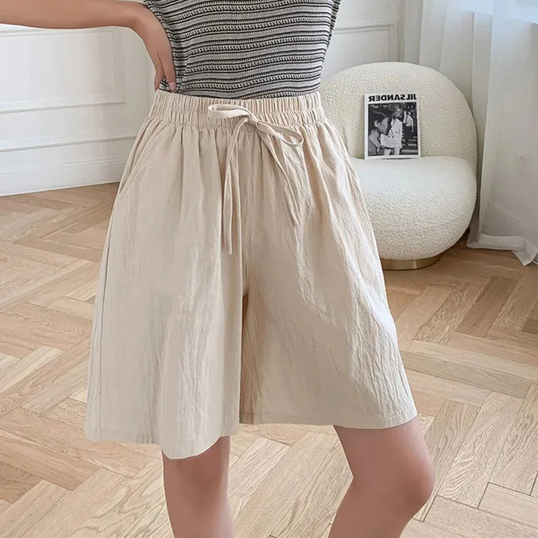 Pantaloncini beige da donna in cotone, vita alta con laccio, indossati con maglietta a righe. Stile casual estivo, moda femminile.