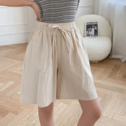 Pantaloncini beige da donna in cotone, vita alta con laccio, indossati con maglietta a righe. Stile casual estivo, moda femminile.