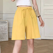 Donna con pantaloncini gialli a vita alta, top bianco corto e borsa a tracolla beige. Stile estivo casual, moda femminile trendy.