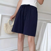 Donna con pantaloncini blu scuro, top bianco e borsa di paglia. Moda estiva casual, abbigliamento femminile elegante e comodo.