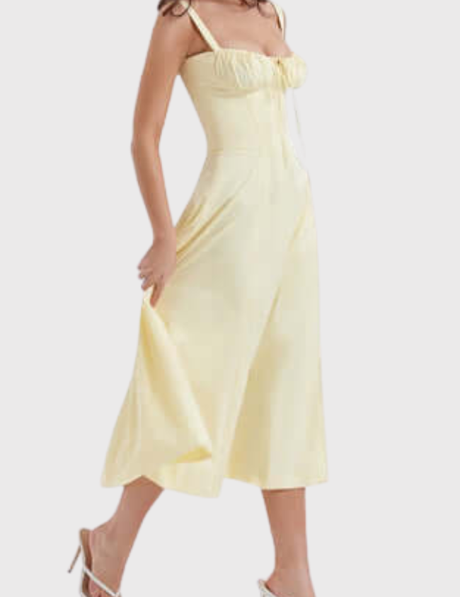 Abito midi giallo chiaro con spalline sottili, scollo a cuore e gonna svasata. Modella indossa sandali bianchi con tacco. Moda estiva elegante.